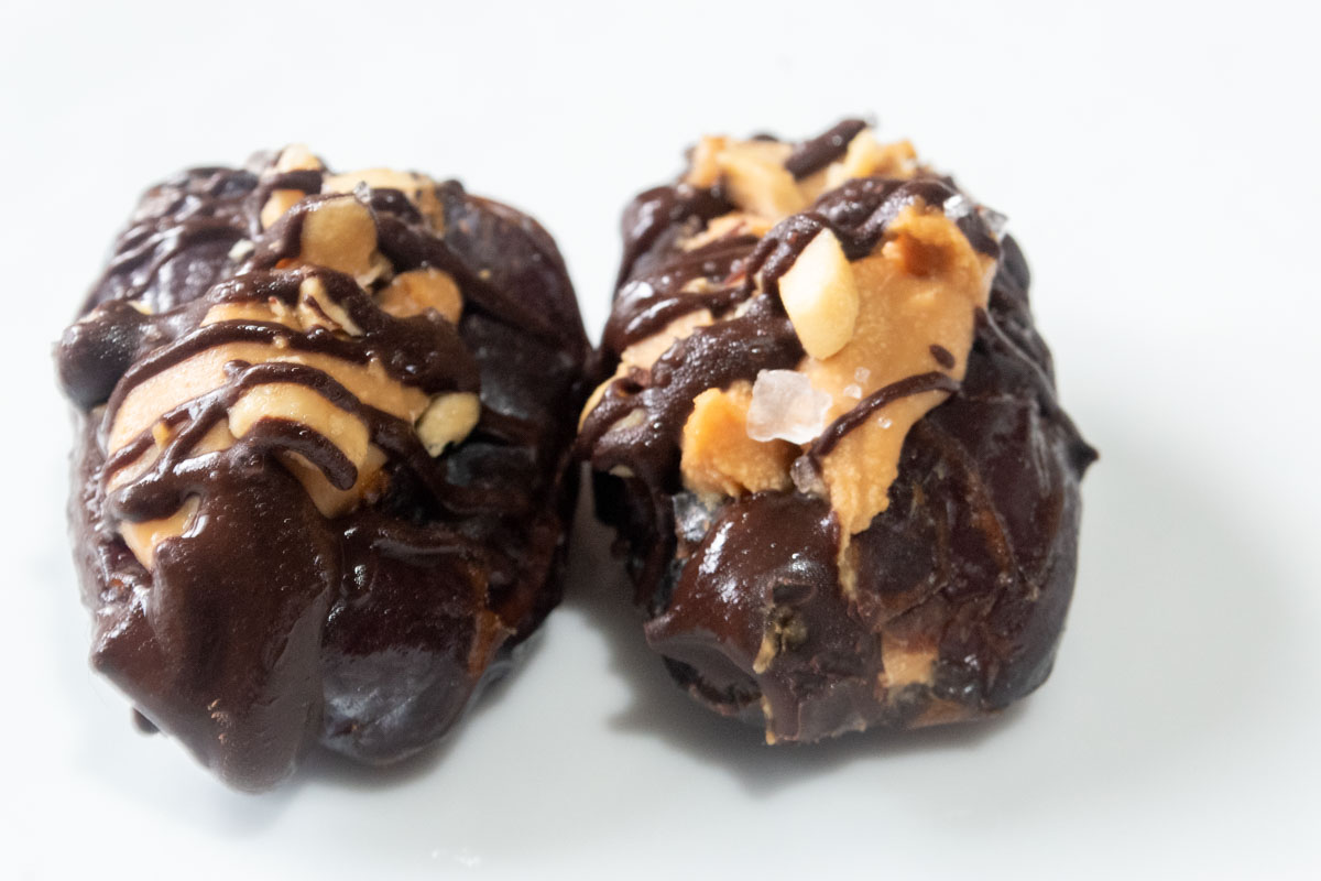 Two stuffed dates on a white board. The chocolate has set on top after being in the fridge.