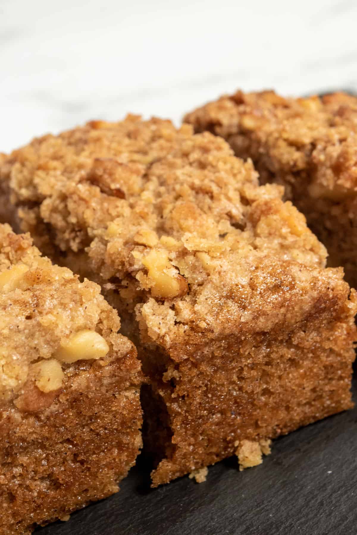 A whole apple cake on a slate platter. It is golden brown and super crumbly. 