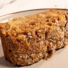 A large slice of vegan apple crumble cake sat on a wide, brown-rimmed plate. You can see the chopped Granny Smith apples inside.