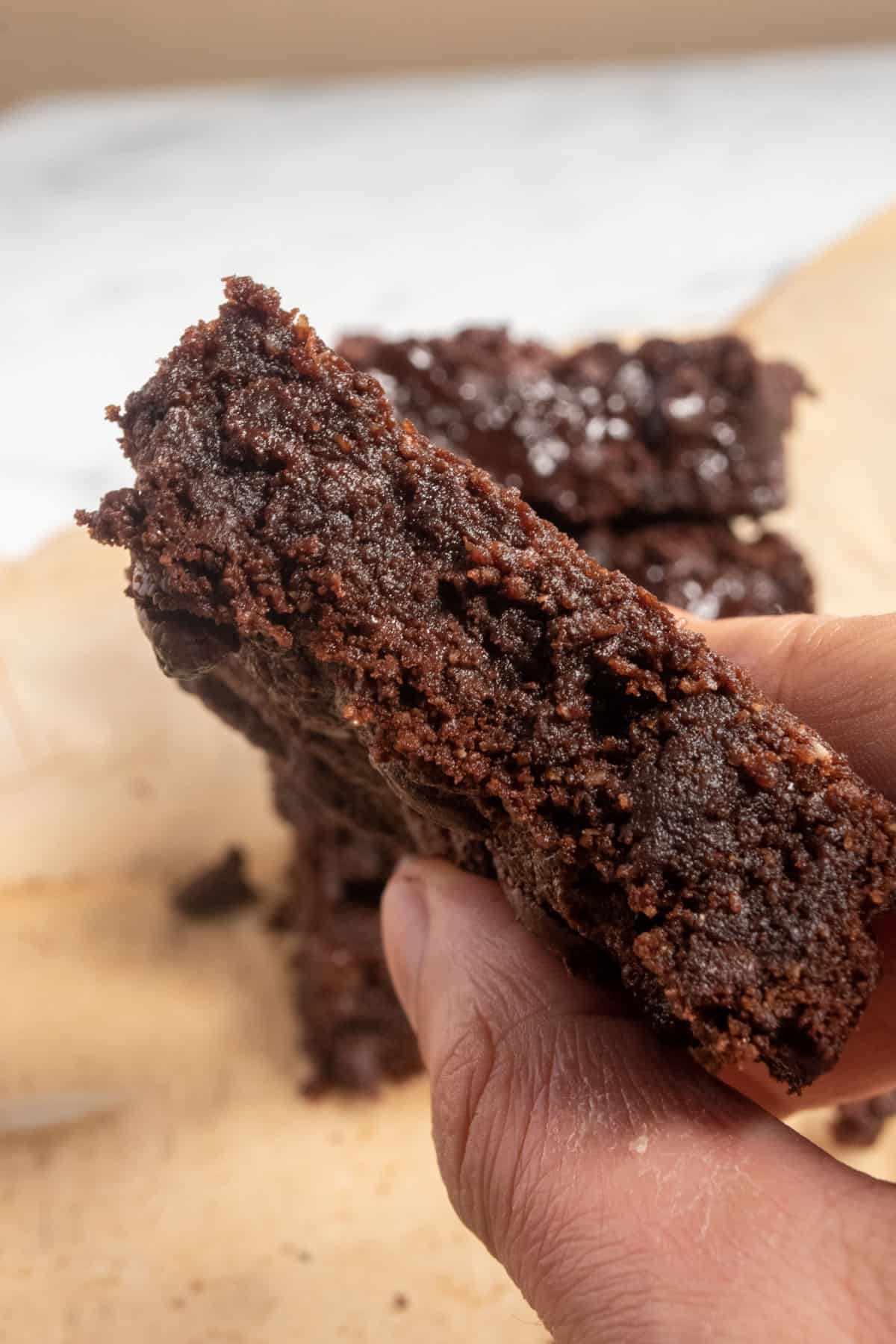 One of my vegan banana brownies being held by a hand, revealing the side of it. It is moist and fudgy. 