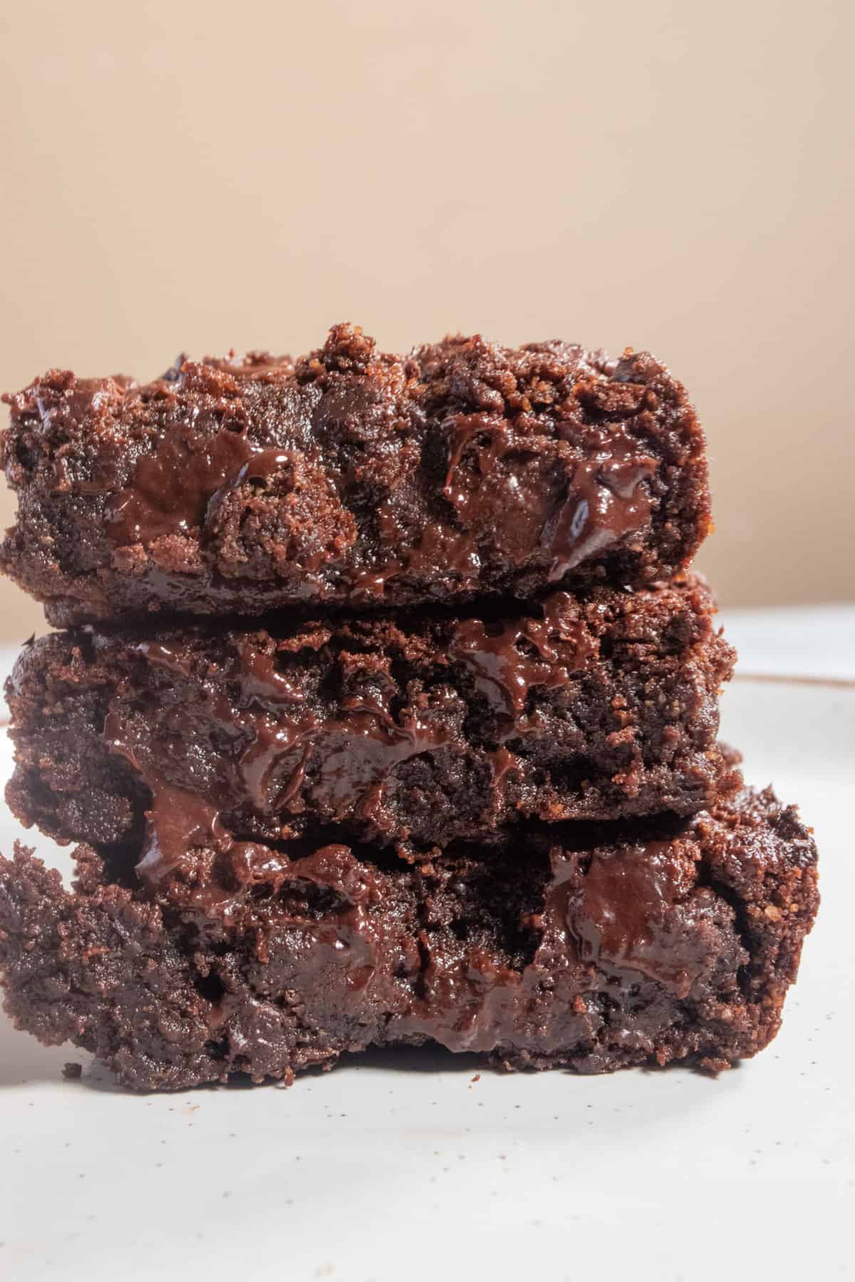 Three chunky  and stacked banana brownies covered with melted vegan chocolate on a large white plate.