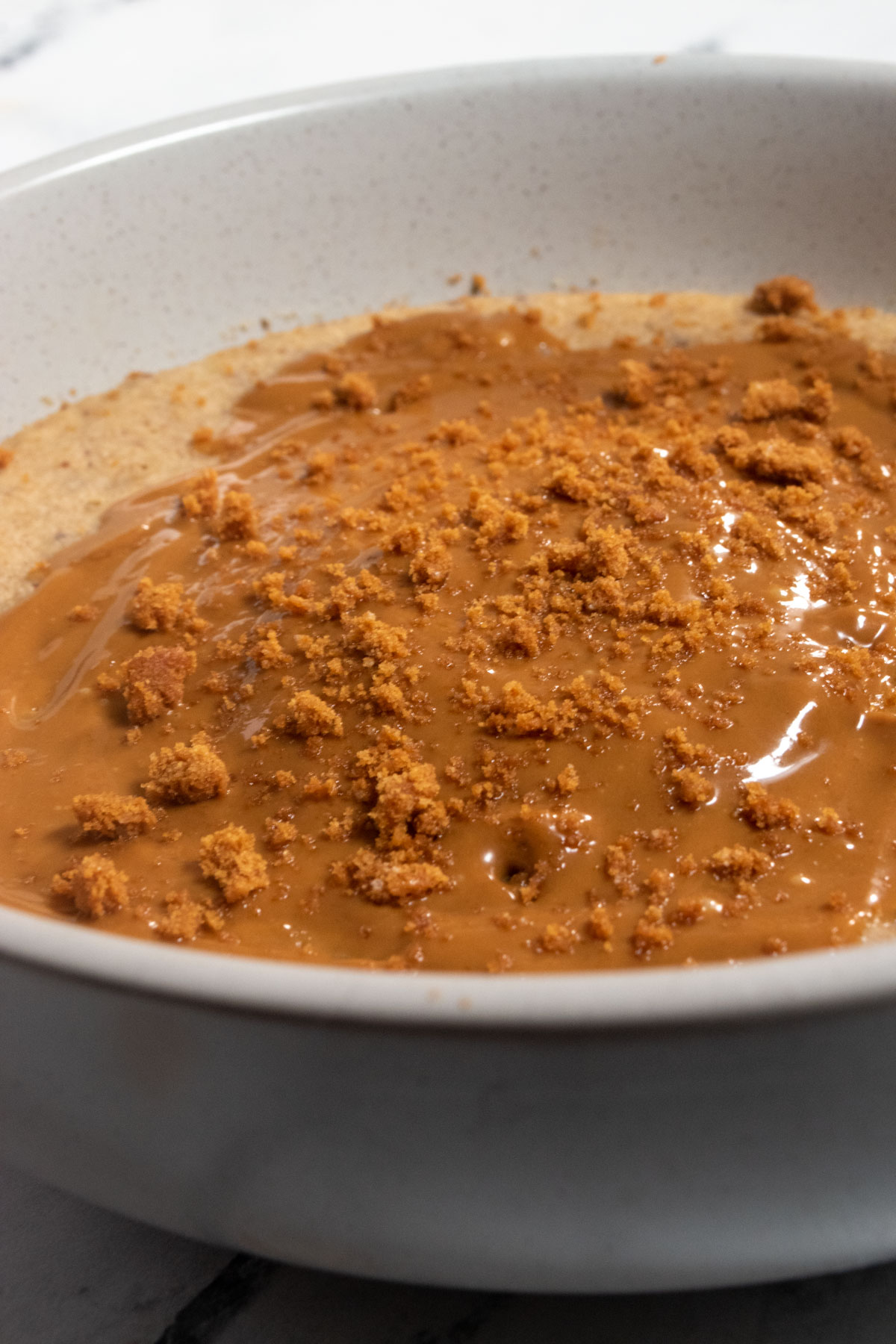 A bowl of my biscoff baked oats. There is plenty of melted biscoff spread on top as well as biscoff cookie crumbs. 