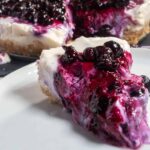 A large creamy slice of vegan blueberry pie on a white plate. The rest of the cream pie is in the background.