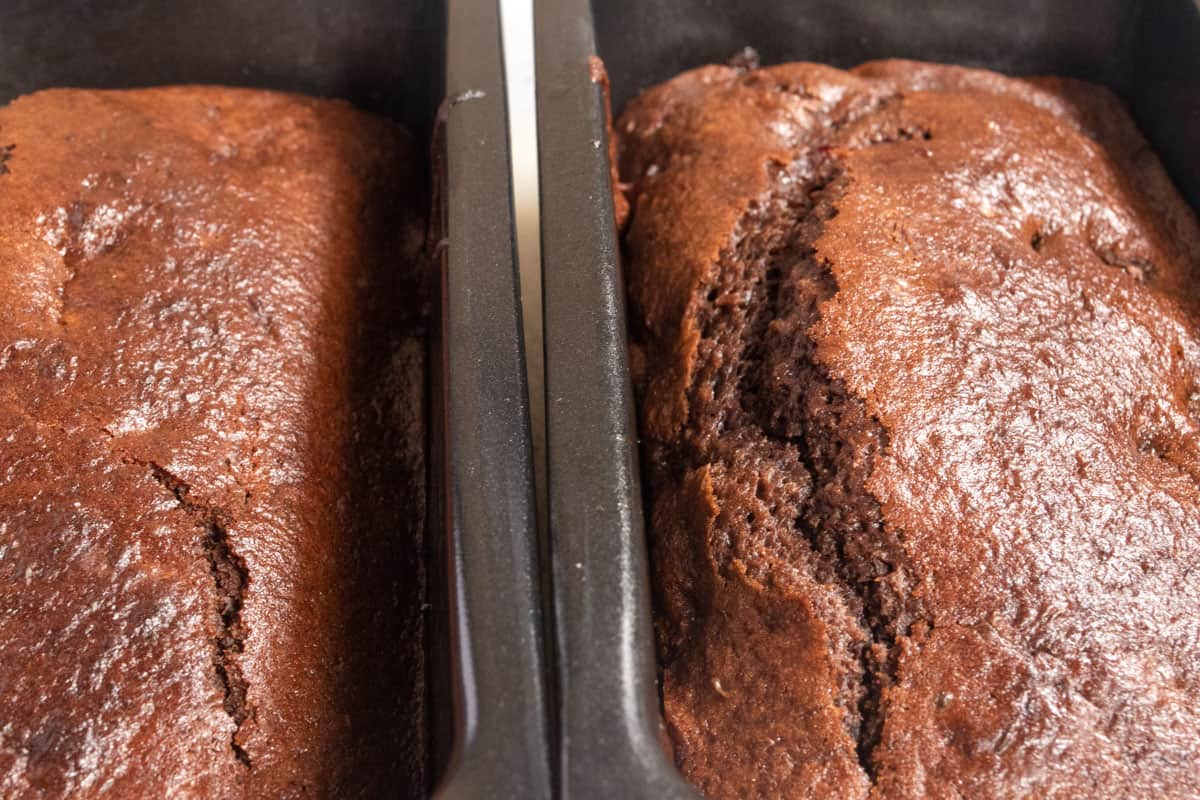 Two baked chocolate cherry loaf cakes cooling down inside their tins.