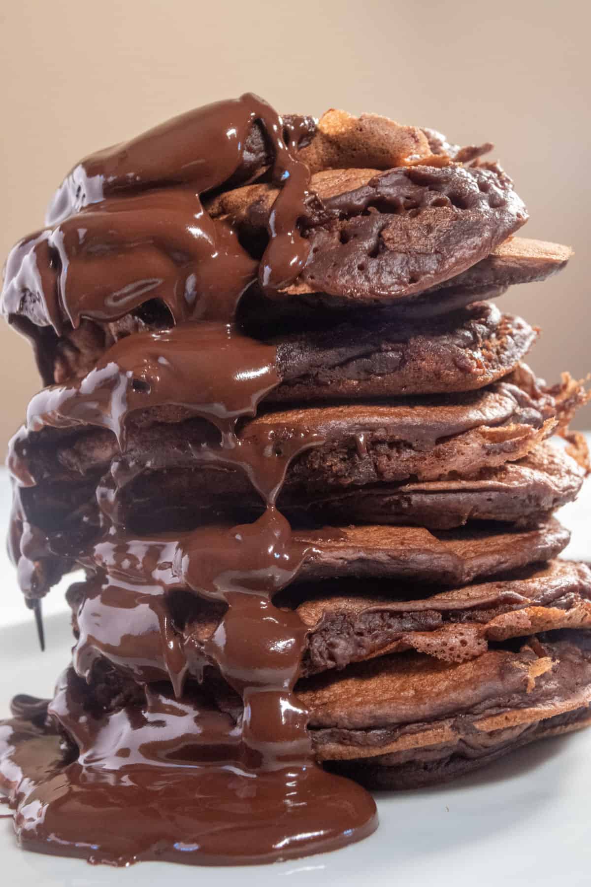 Chocolate covering a stack of pancakes generously. There is a pool of melted chocolate on the plate.