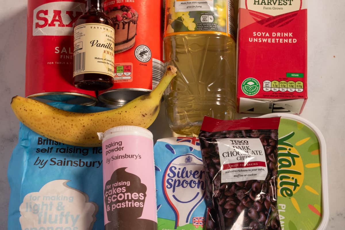 The ingredients that you need to make vegan chocolate chip pancakes laid out neatly over a white, marble background. 