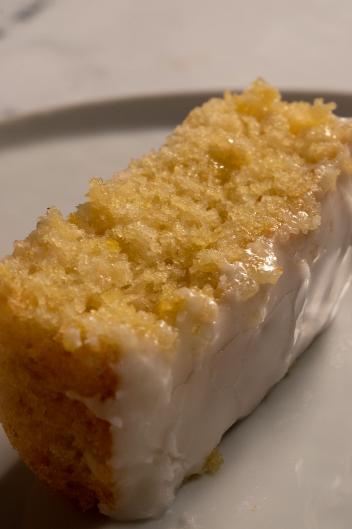 A chunky slice of lemon cake on a shiny, white plate. It's golden and moist.
