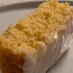 A large slice of vegan lemon olive oil cake on a white plate. It is moist and soft.