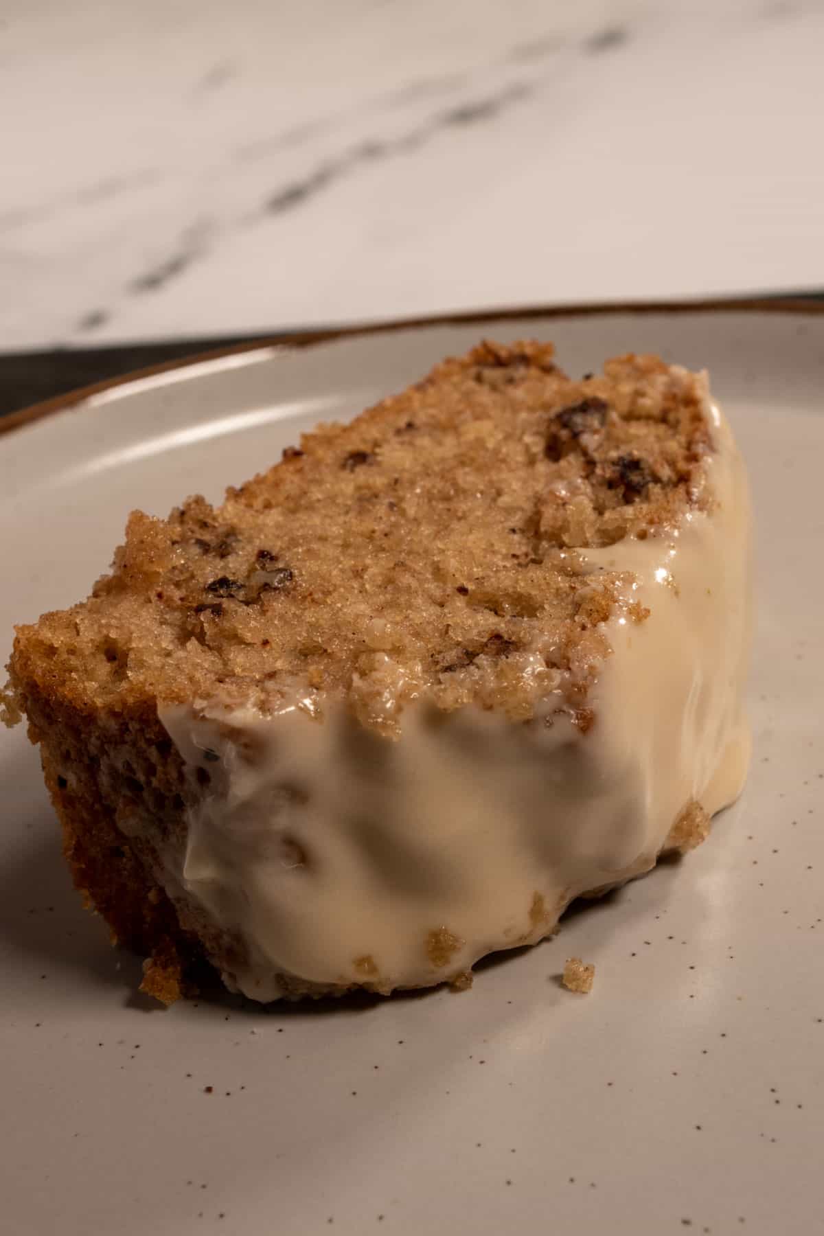 A large slice of cake on a brown-rimmed plate. The crumb is golden brown. There are lots of pecans inside. 