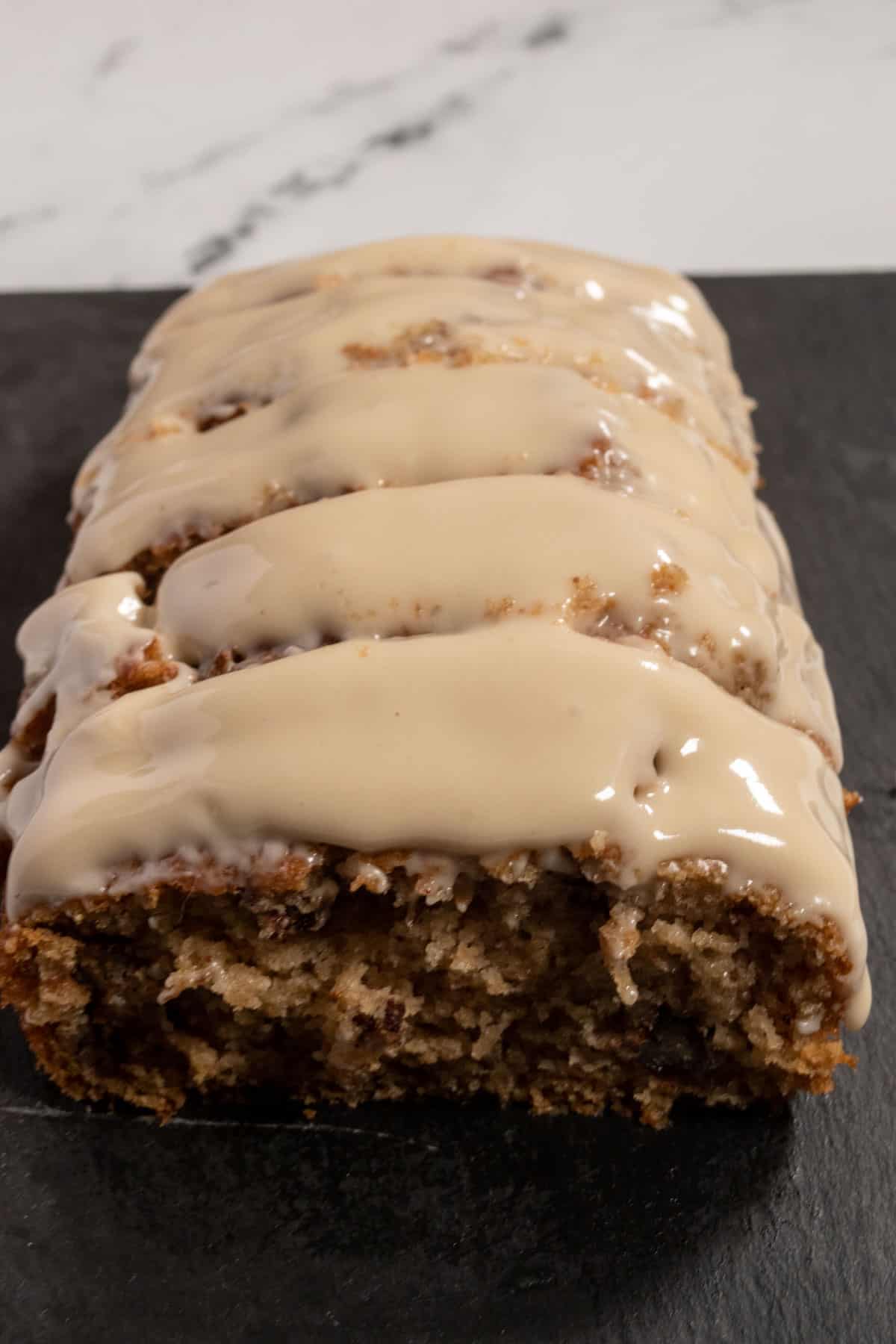 A whole loaf of maple pecan cake on a black slate platter. It is covered in thick maple glaze.