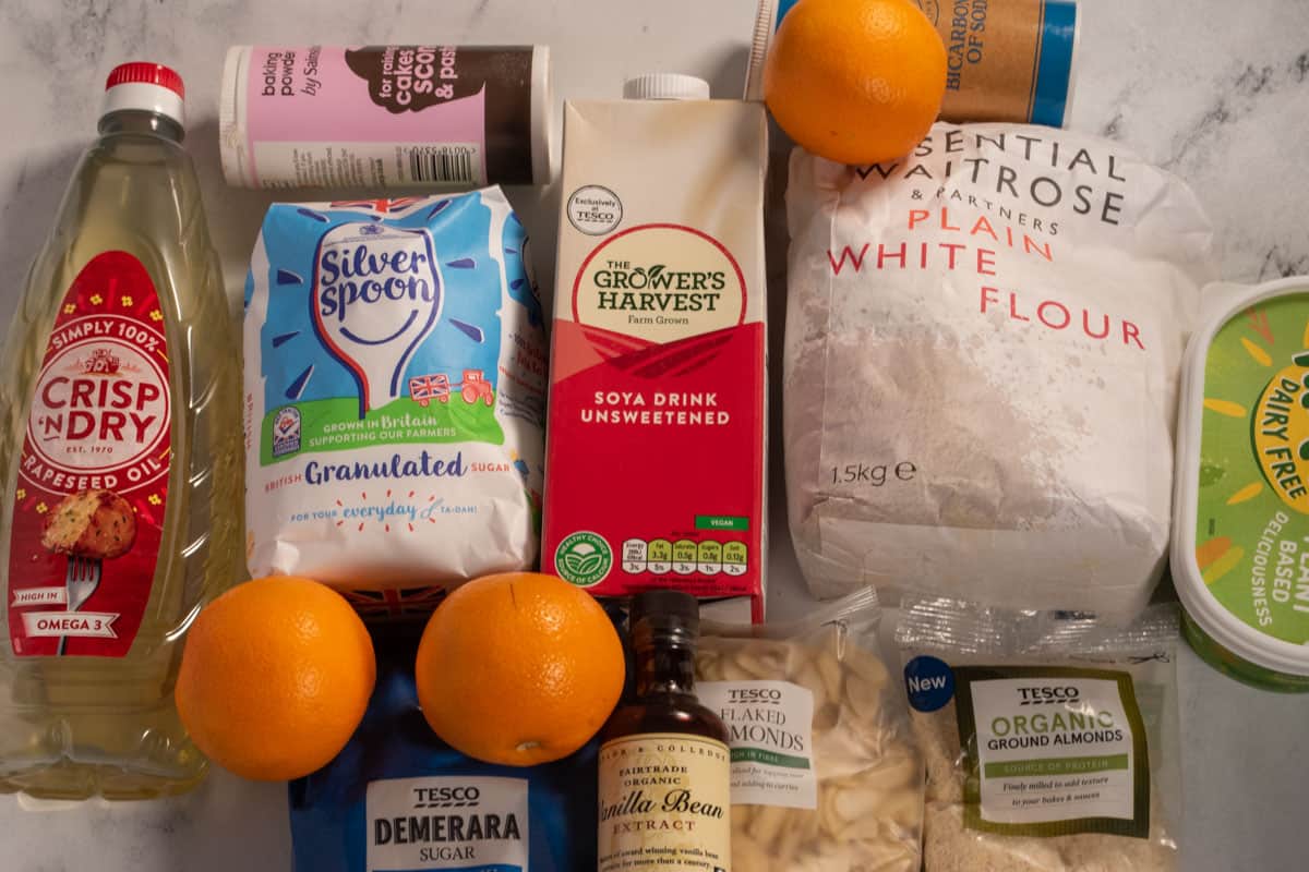 The ingredients that you need in order to make my vegan orange almond cake laid out over a white, marble background.