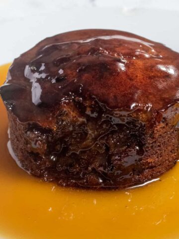 A whole vegan sticky toffee pudding covered in a pool of vegan toffee sauce.