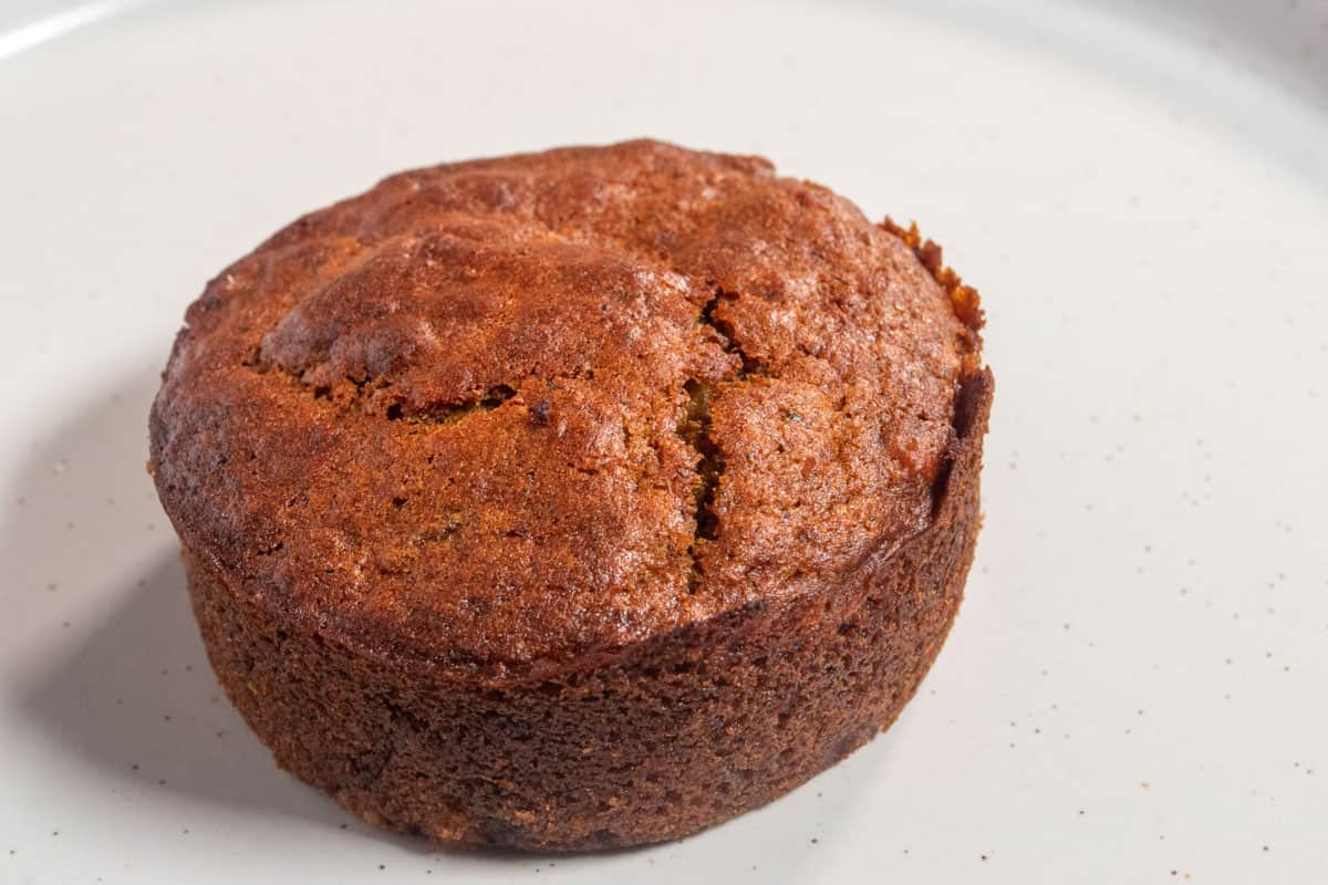 A baked vegan sticky toffee pudding cake on a white plate waiting to have sauce poured over it.