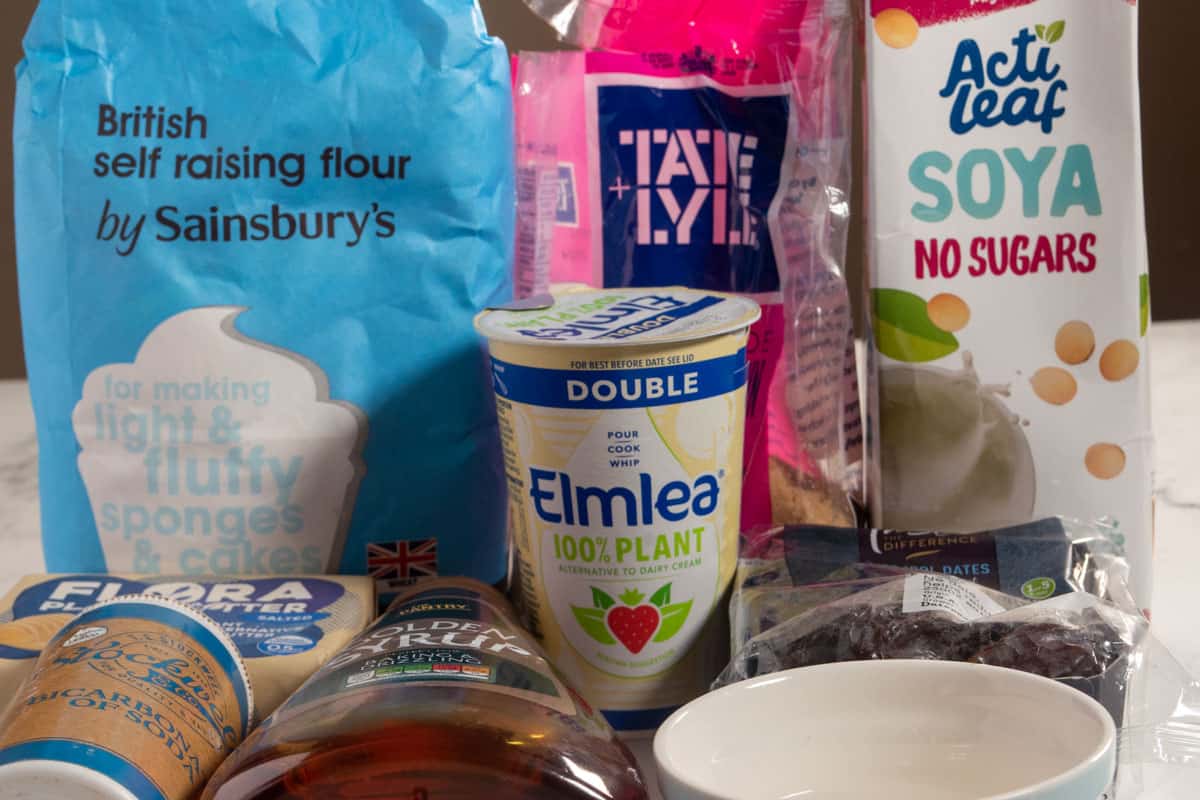 The ingredients that you'll need to make vegan sticky toffee pudding laid out neatly over a white, marble backdrop. 