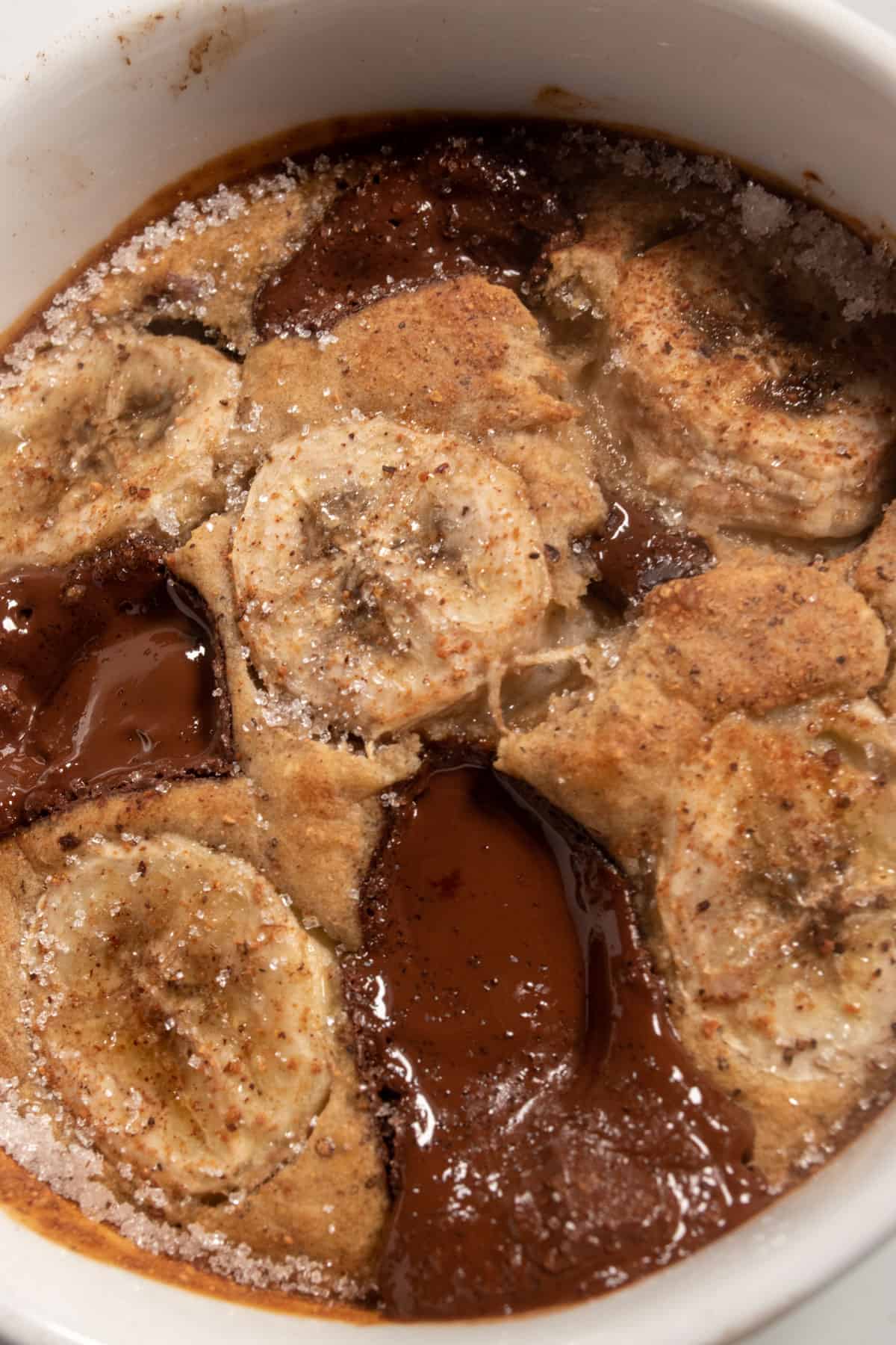 A large portion of vegan banana bread baked oats inside a shiny white ramekin. The bananas on top are toasted and the chocolate has melted.