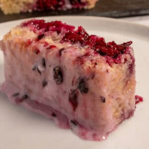 A chunky slice of blackberry lemon cake sitting on a glossy, white plate.