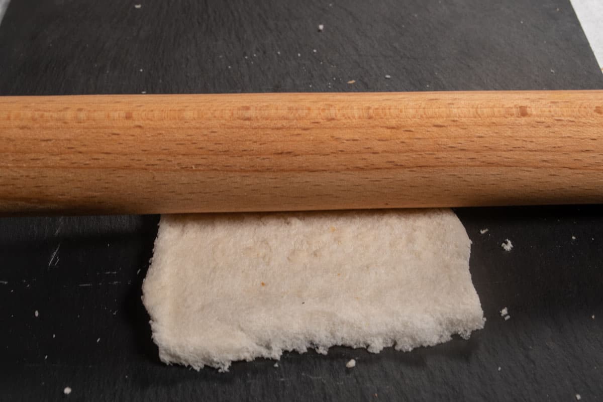 The slice of bread being flattened with a rolling pin. 