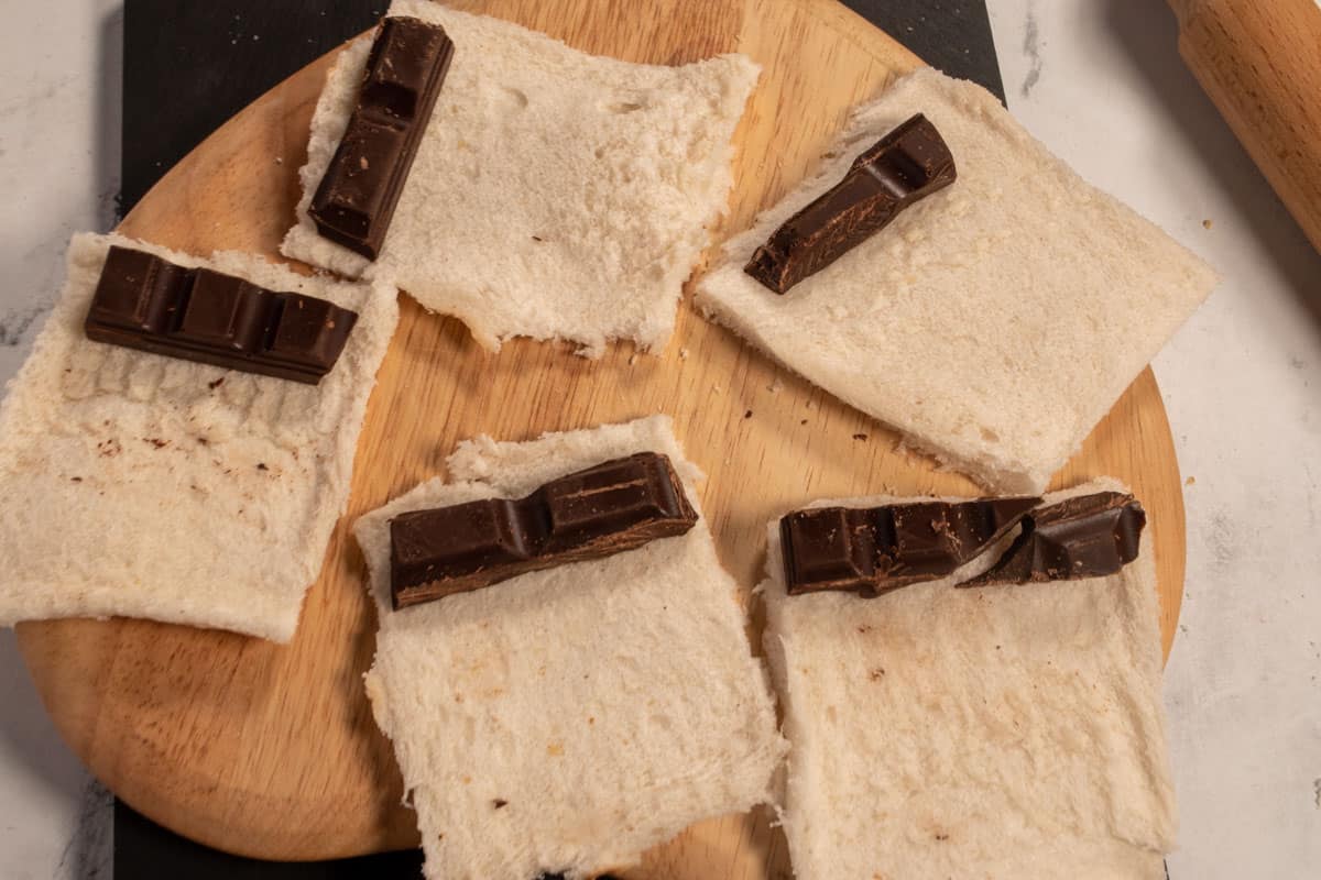 Thin pieces of chocolate have been placed on the edge of each slice of bread, ready to be rolled. 