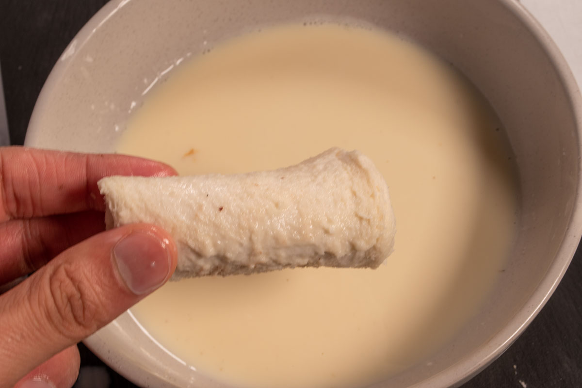 A hand holding a french toast roll after it has been dipped. 