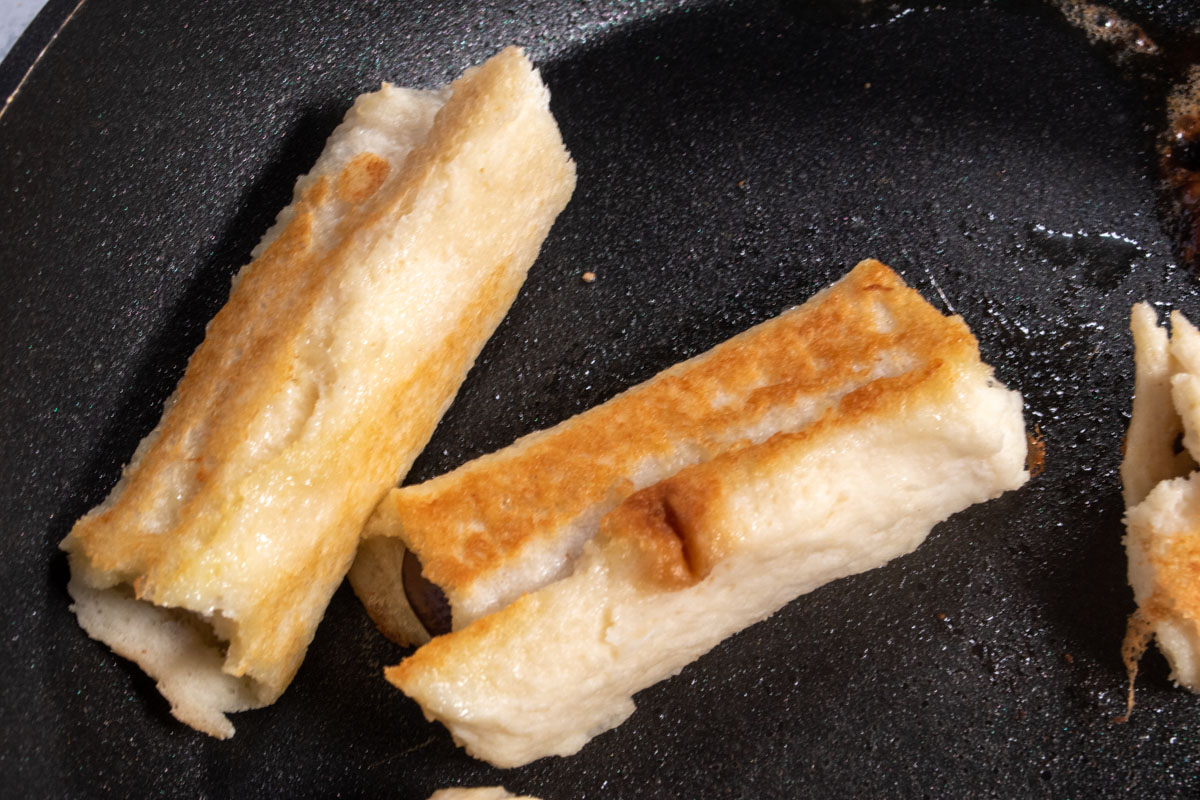 Golden brown rolls cooking inside a black frying pan. 