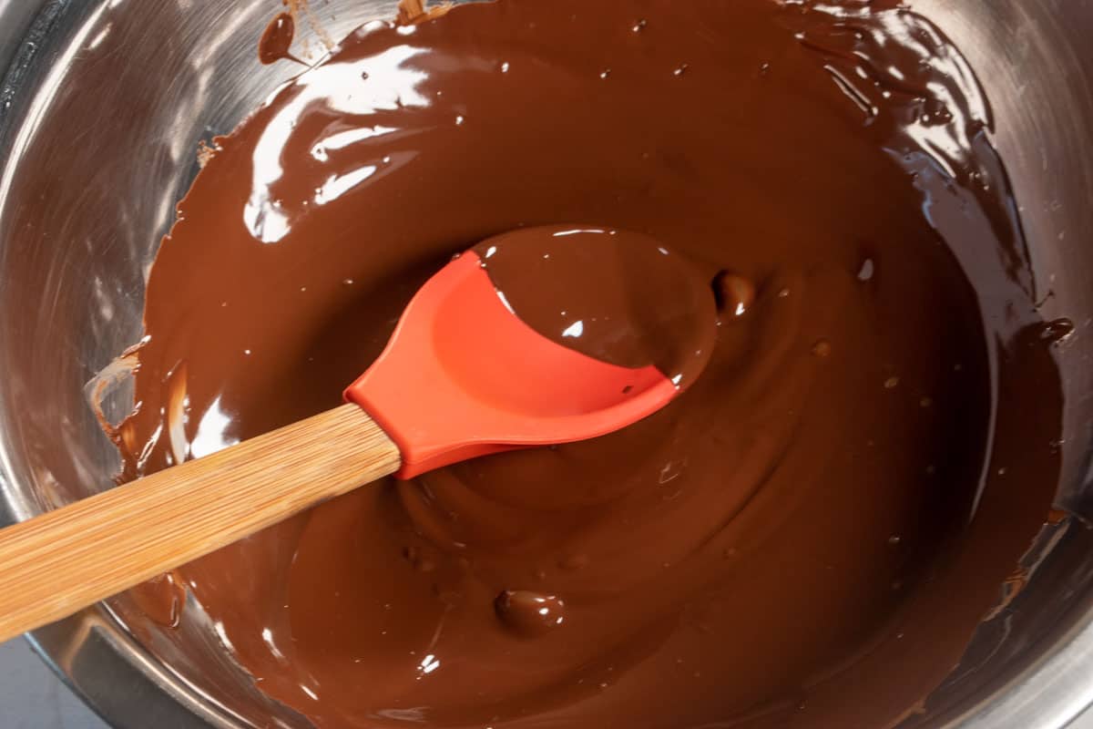 Melted chocolate being stirred inside a large metal mixing bowl. 