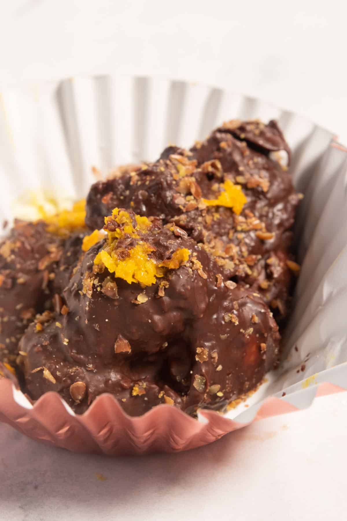 A uneven chocolate cluster which has been sprinkled with bright orange zest sitting in a large cupcake liner.