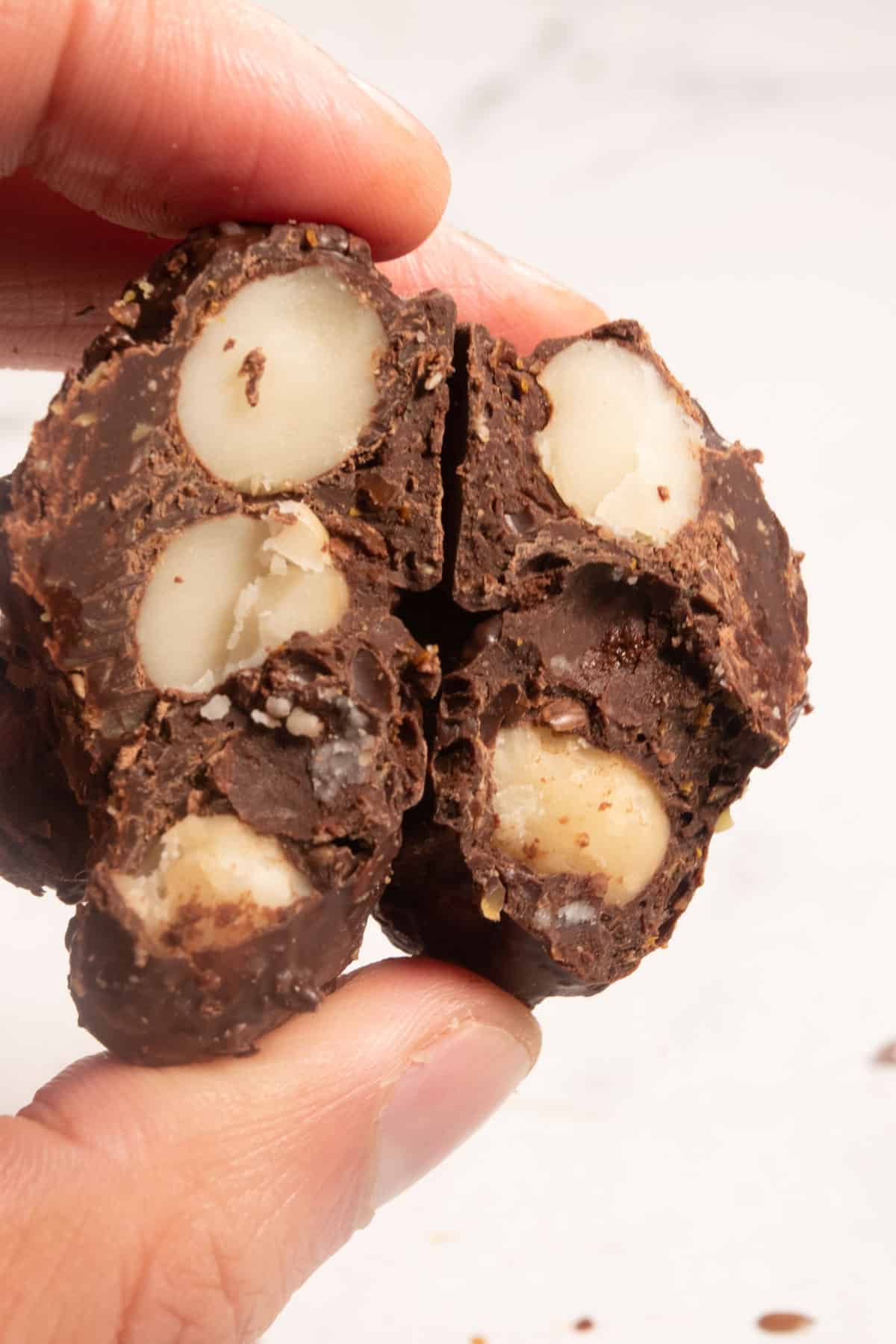 A cluster which has been broken in half being held in a hand. There are lots of macadamia nuts inside. 