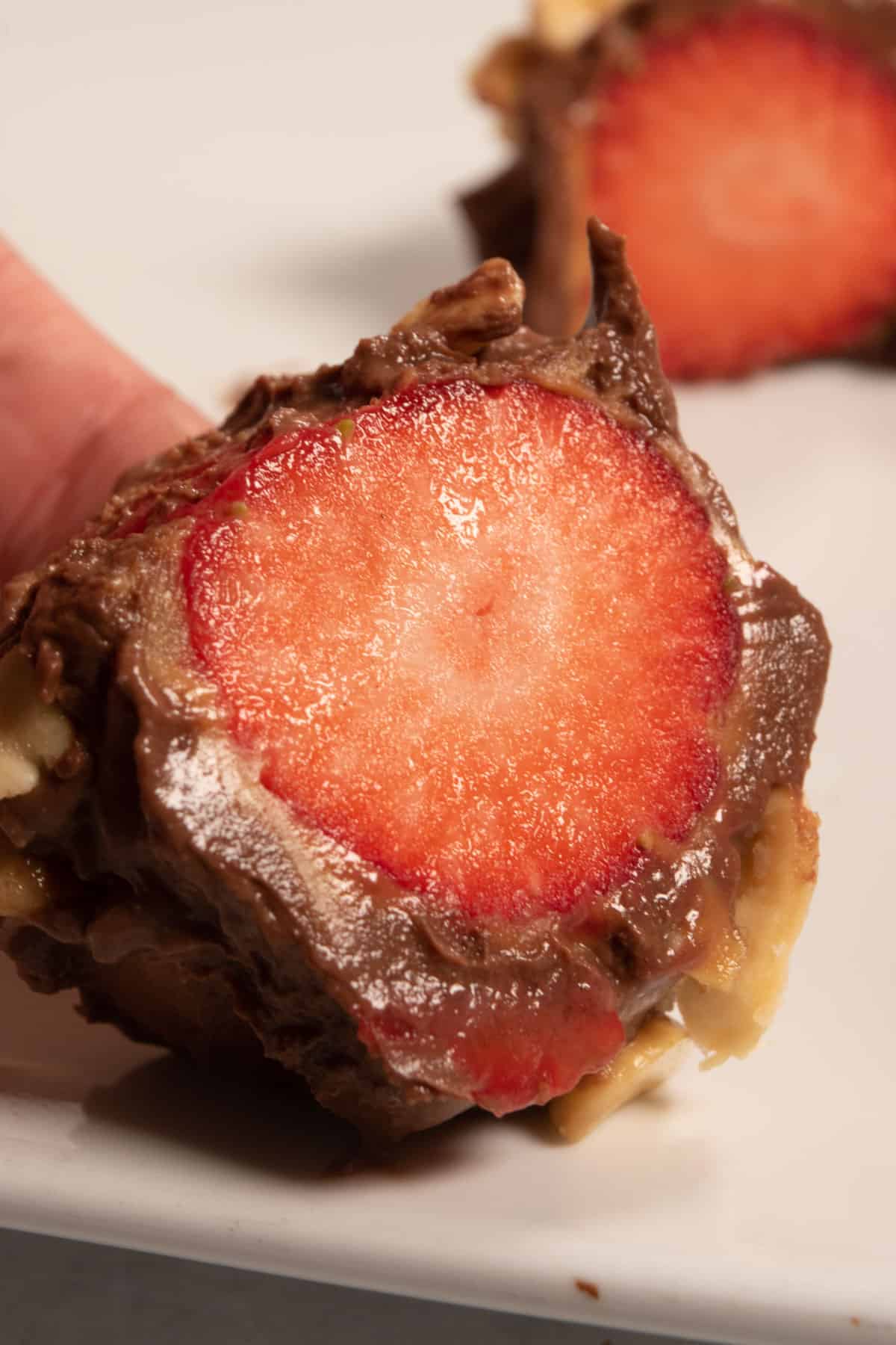 A hand holding a frozen yogurt strawberry bite which has been sliced open revealing the fruit inside. 