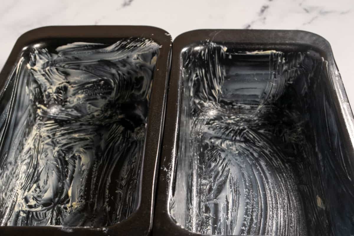 Two black cake tins, which have been greased with vegan butter. 
