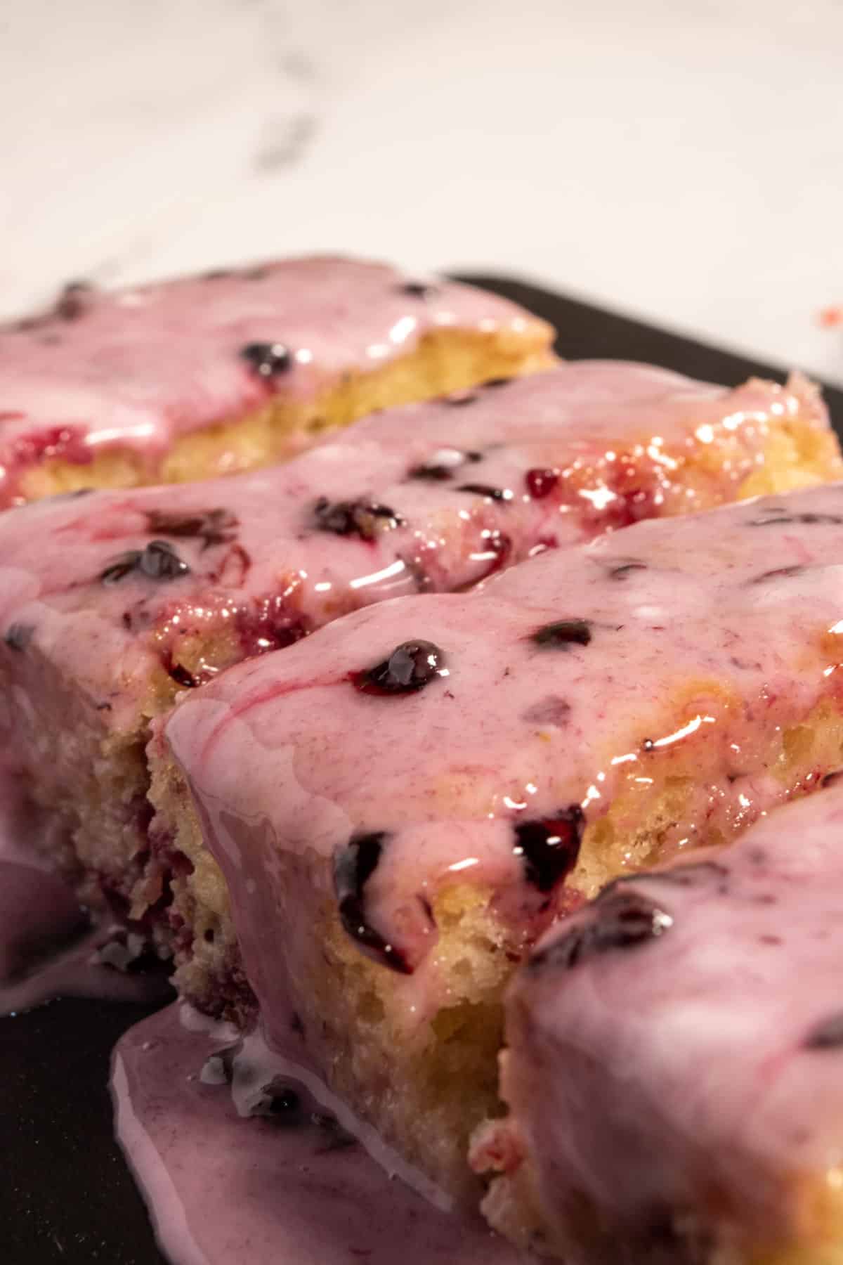 A side angled photo of an entire vegan blackberry cake on a slate chopping board. 