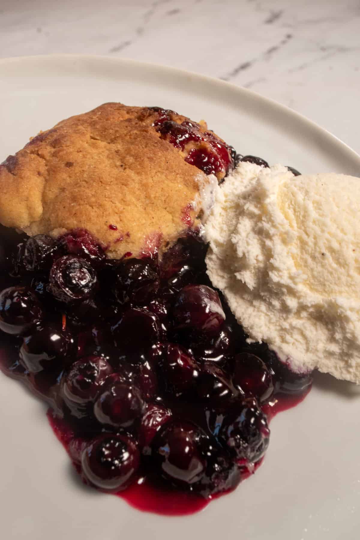 The cobbler batter, filling and vegan vanilla ice cream combined on a white plate.