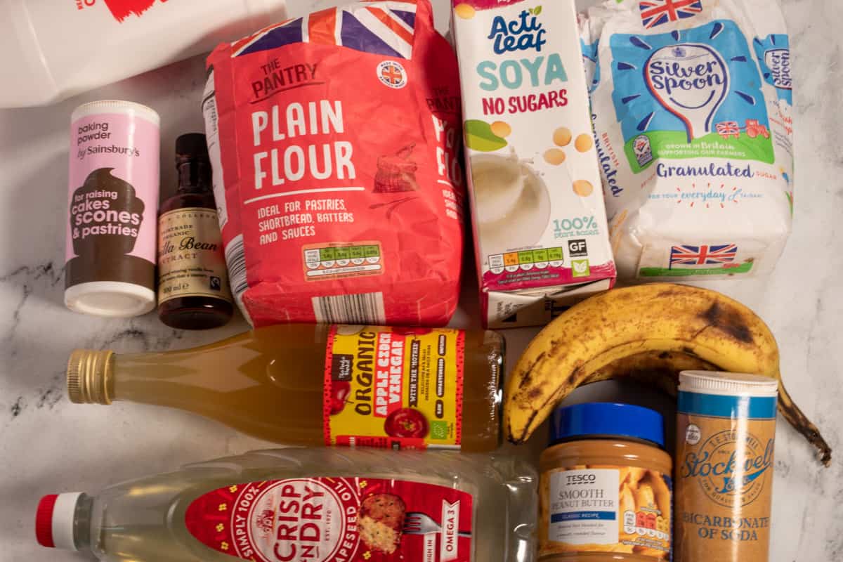 The ingredients that you will need in order to make my vegan peanut butter banana cake laid out over a white, marble background.