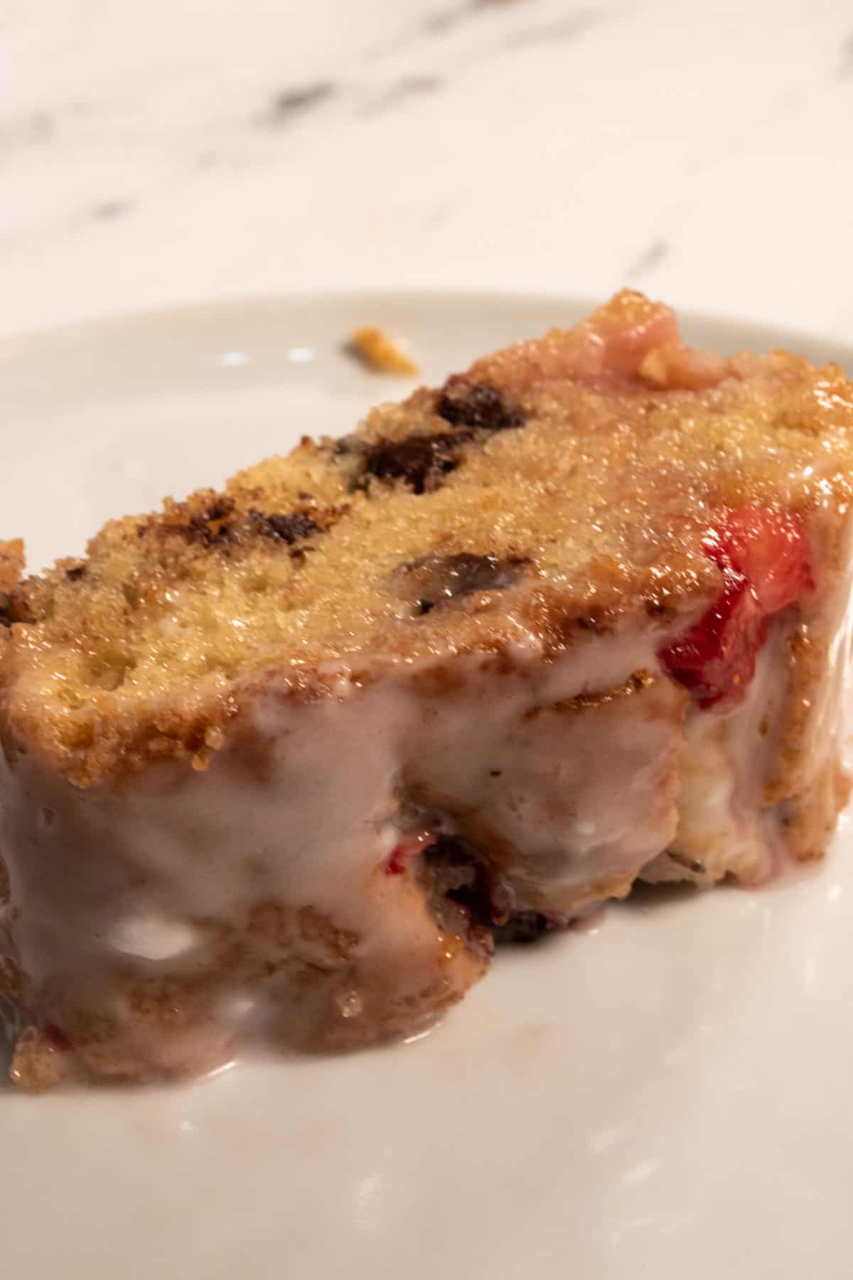 A long piece of strawberry cake which is full of chocolate chips on a white plate. 