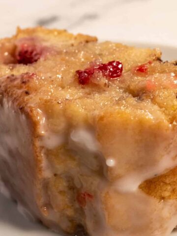 A close up shot of a thick slice of vegan strawberry cake. It is golden brown and filled with bright red strawberries.
