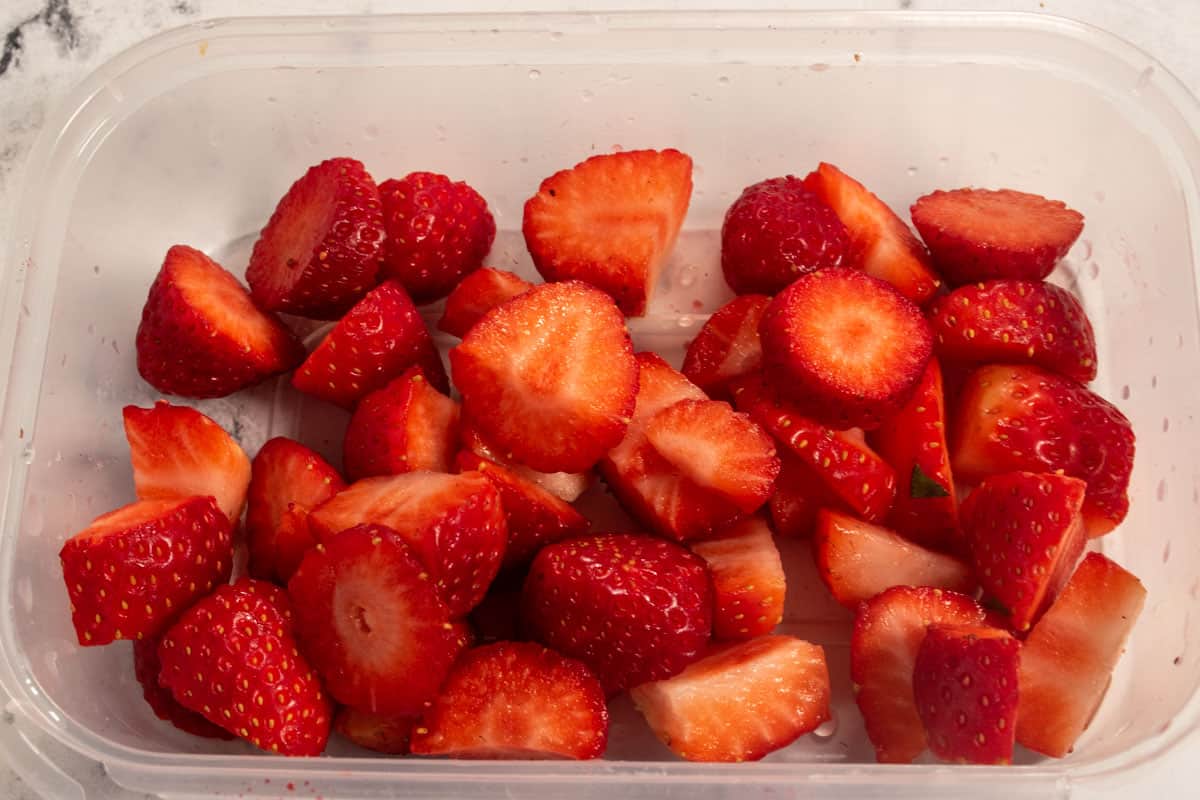 Strawberries inside a plastic container with the tops removed and sliced into even pieces. 