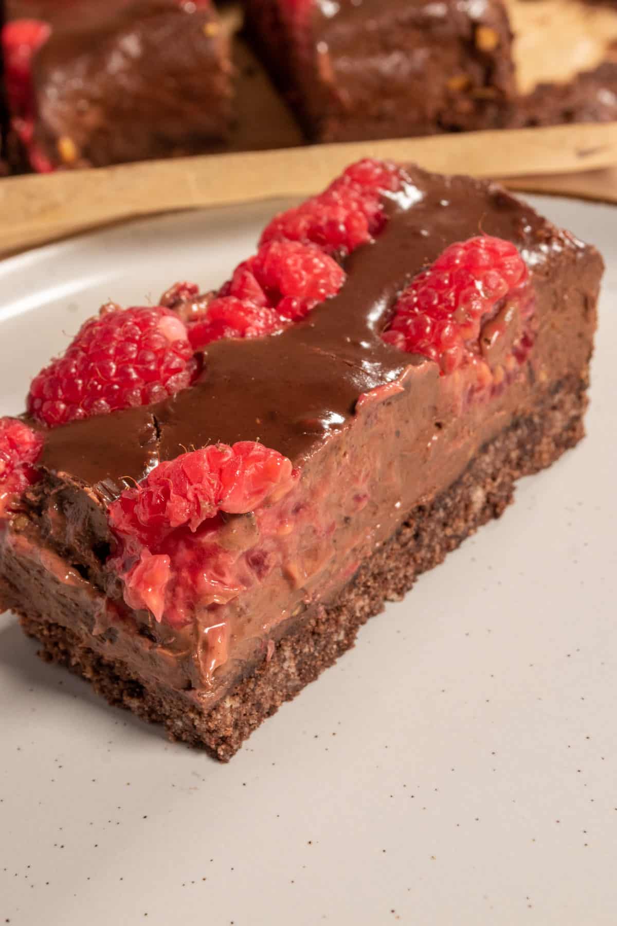 A creamy, chocolatey bar on a white plate. It's topped with bright pink fresh raspberries. 