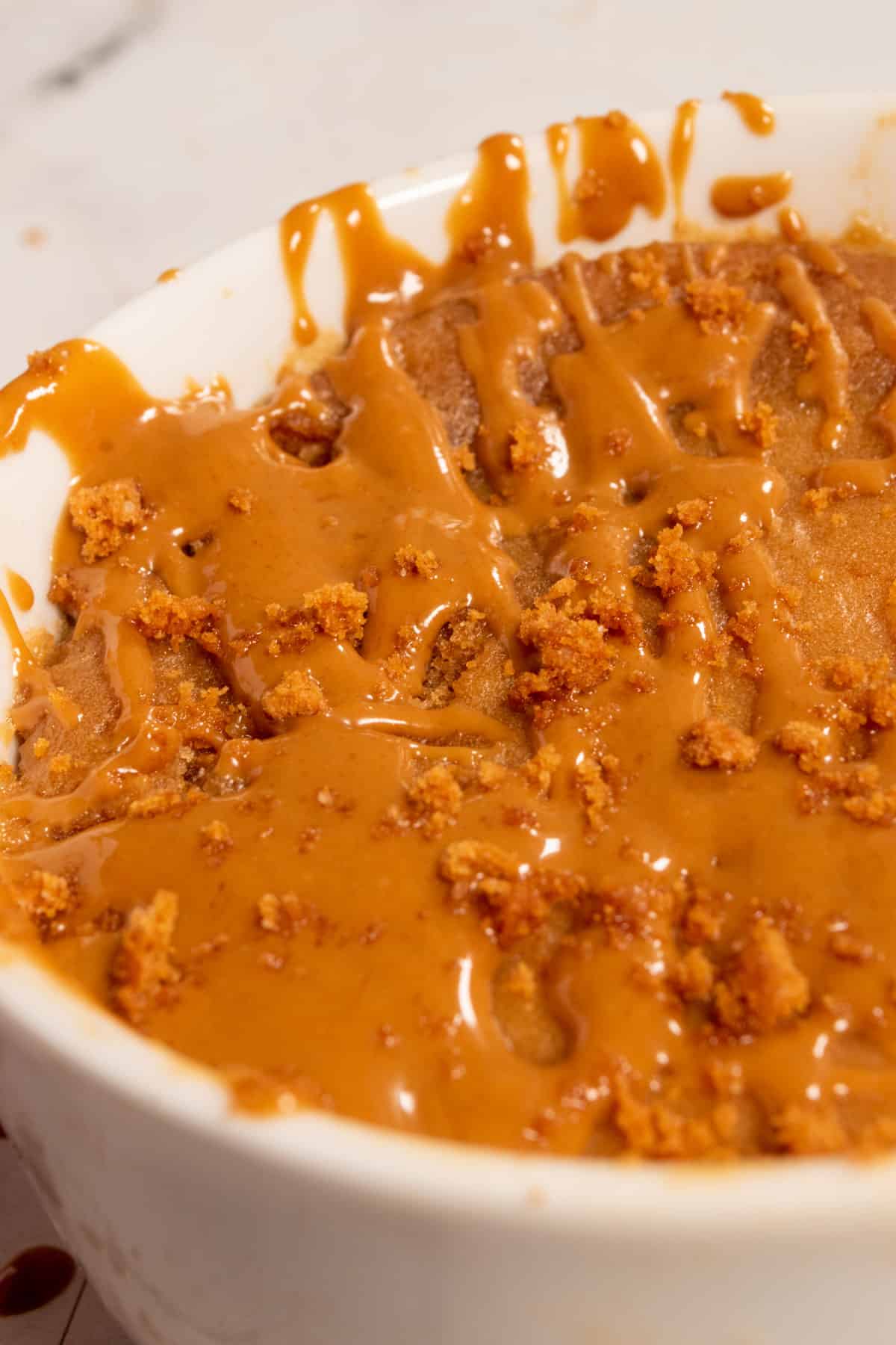 A golden brown-colored Biscoff mug cake inside a white ramekin cooling down.