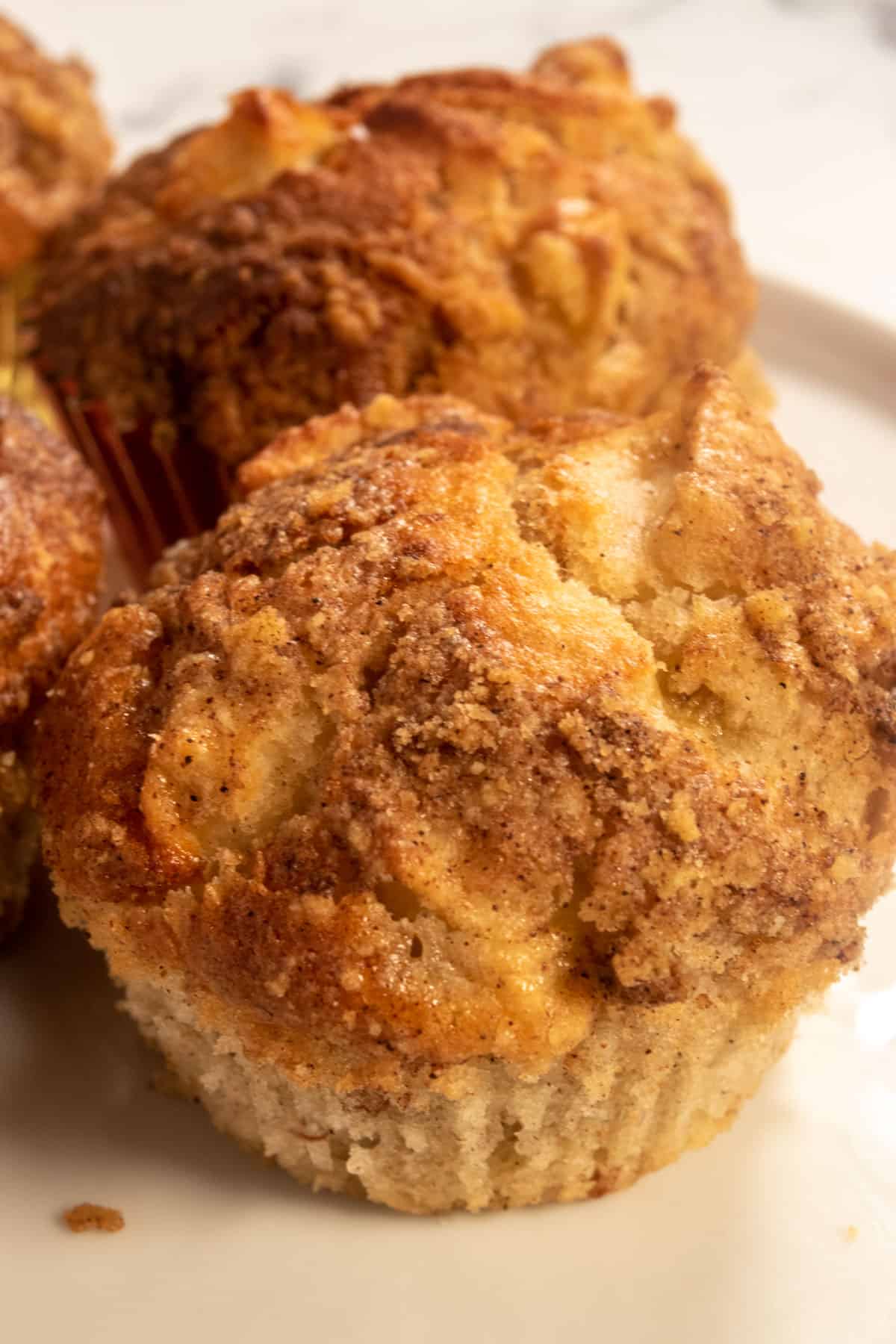 A plate full of golden brown vegan apple cinnamon muffins with lots of streusel on top. 