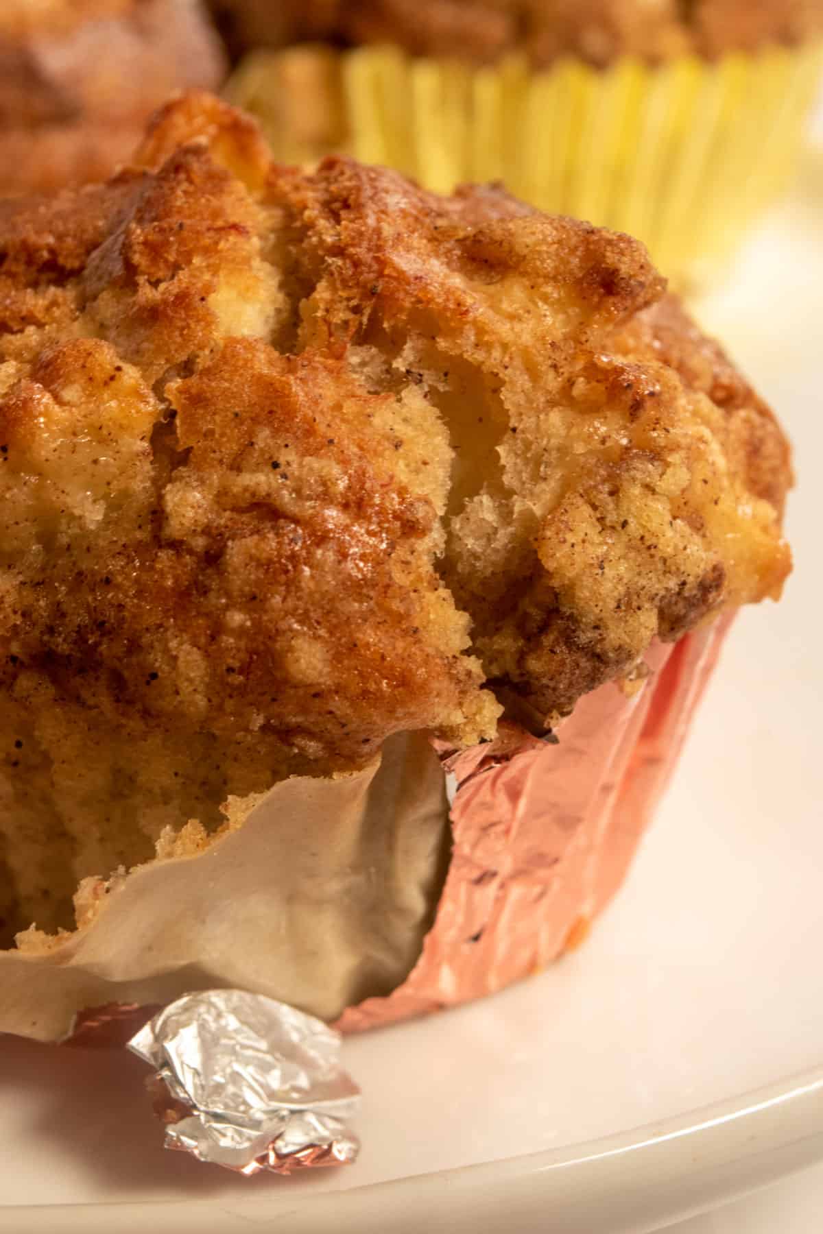 A large muffin which are is sat cooling inside a metallic cupcake liner. More are in the background.