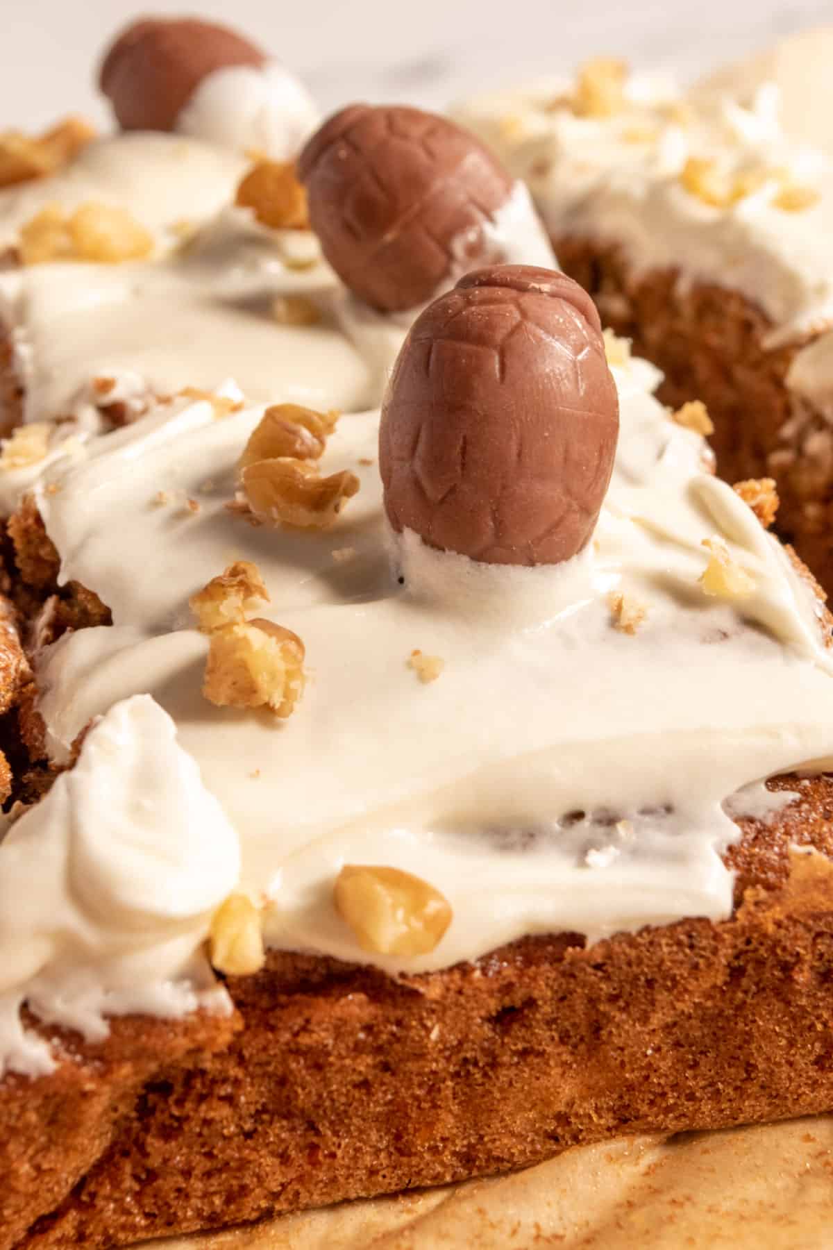 Many vegan carrot cake slices are topped with mini chocolate easter eggs and chopped walnuts.