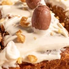 A close up image of decorated vegan carrot cake bars which are topped with dairy free chocolate eggs and chopped walnuts.