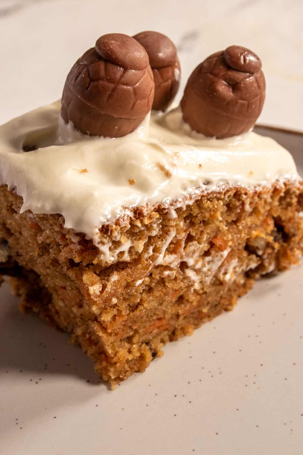 A single piece of carrot cake on a white plate. Three chocolate eggs have been placed on top. 