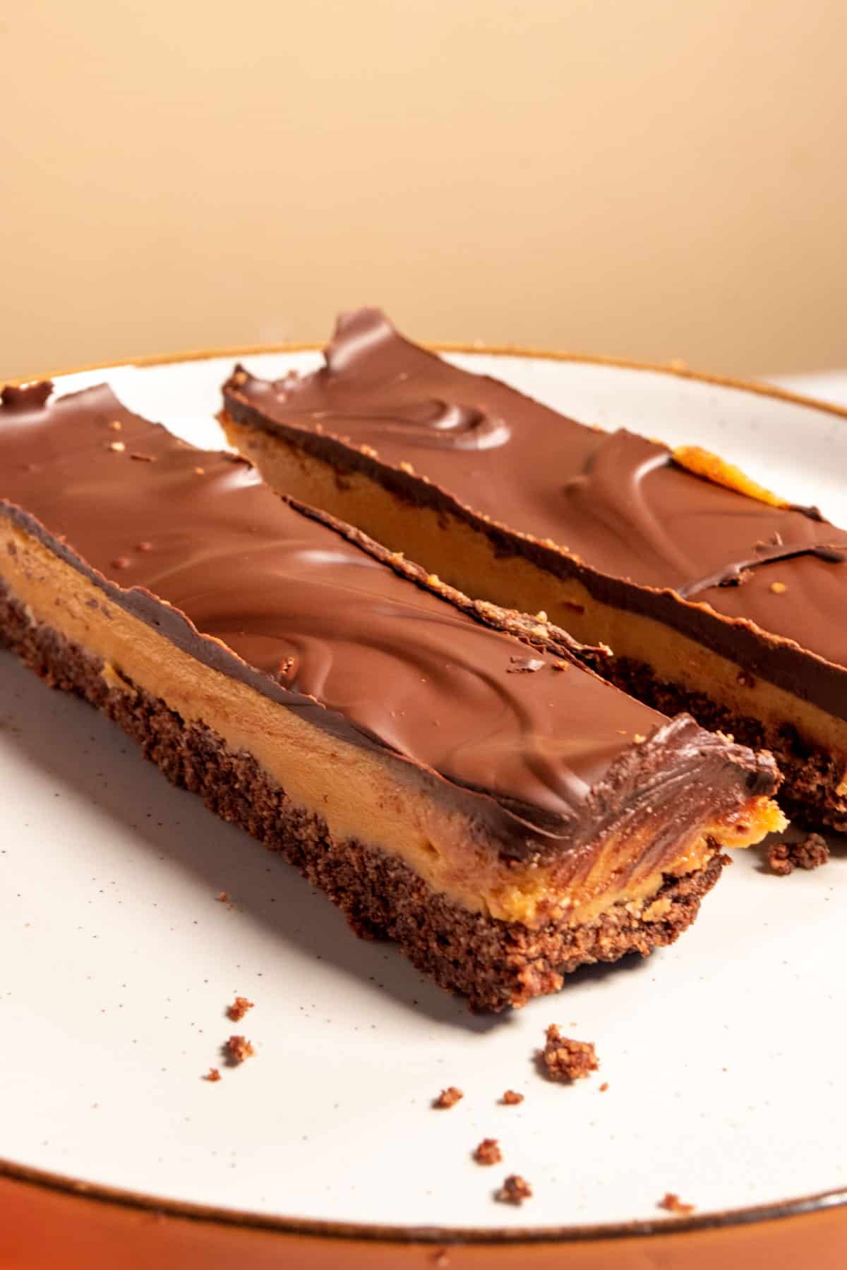 Two vegan chocolate peanut butter bars on a brown-rimmed plate. They're long, thin and shaped like a chunky superstore chocolate bar.