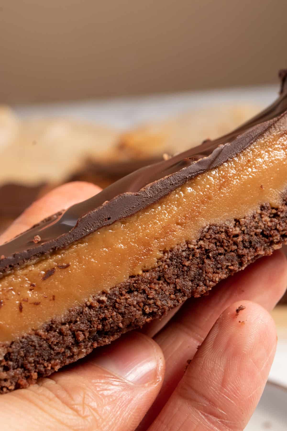 One of my vegan chocolate peanut butter bars being held by a hand. The peanut butter looks gooey in the center of the bar.