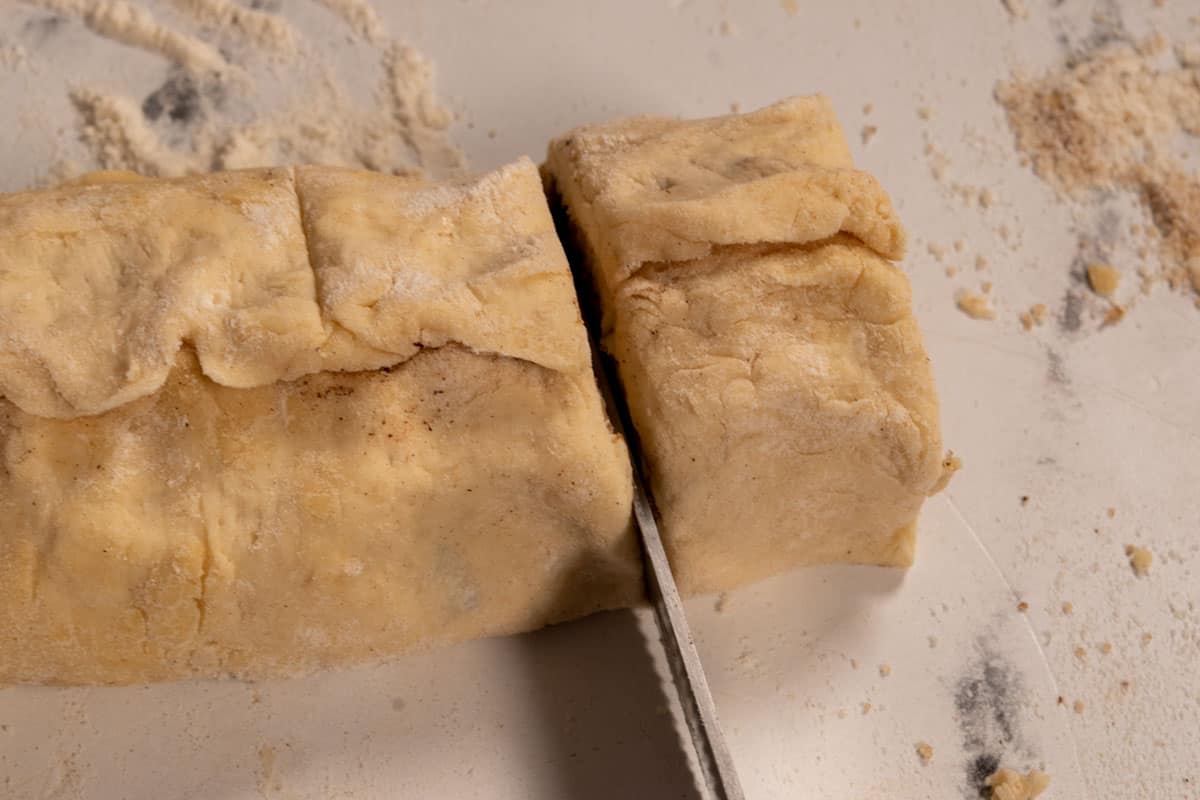 The long dough is being sliced into individual rolls.