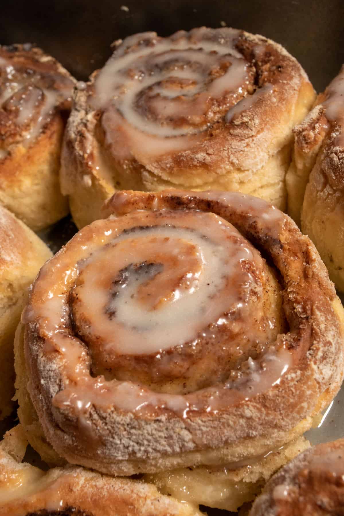 Many golden and toasty vegan cinnamon rolls huddled together in a small space which are topped with lots of glaze.