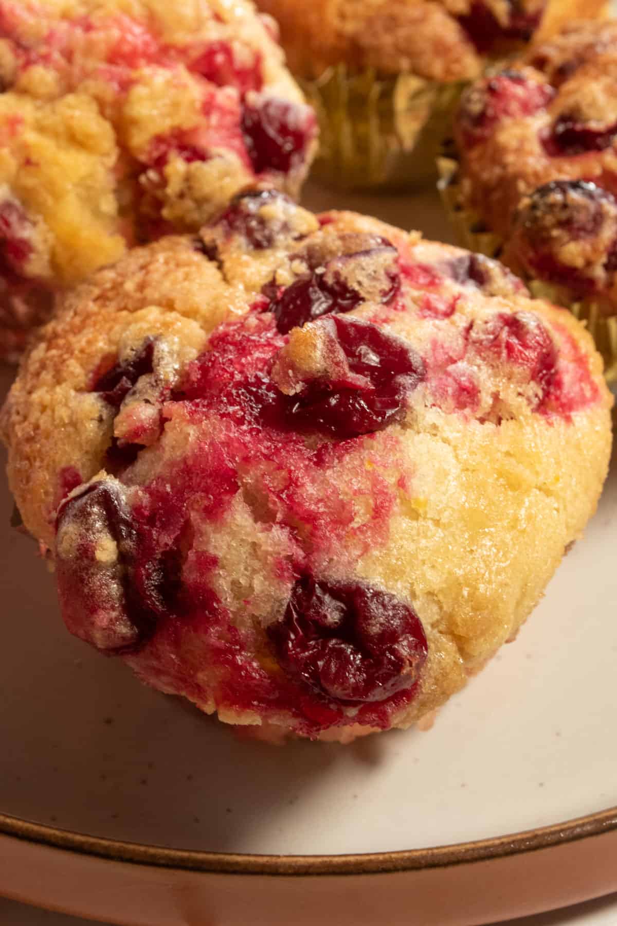 A bunch of large cranberry orange muffins revealing all the detail on top of them. The cranberries are glowing and the muffins are golden.