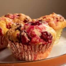 Three golden cranberry muffins on a brown serving plate.