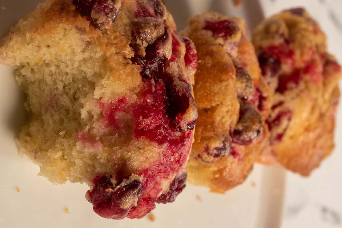 Three baked vegan cranberry orange muffins cooling down on a white plate. 