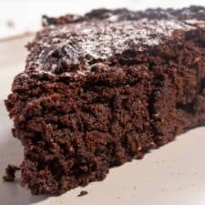 A thick slice of my fudgy flourless chocolate cake on a white and brown plate.